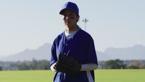 Portrait-of-mixed-race-female-baseball-player-wearing-eye-black,-throwing-ball-into-glove