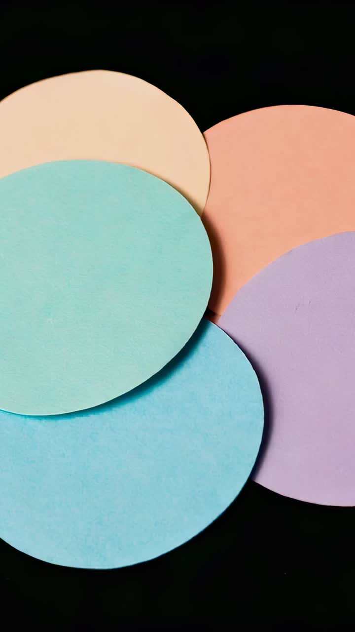 Vertical video: Hand pushing five pastel circles rolling off black studio surface, with craft theme