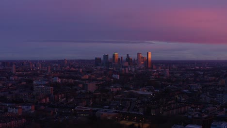 dolly back aerial drone shot from canary wharf skyscrapers over residential area london at sunset