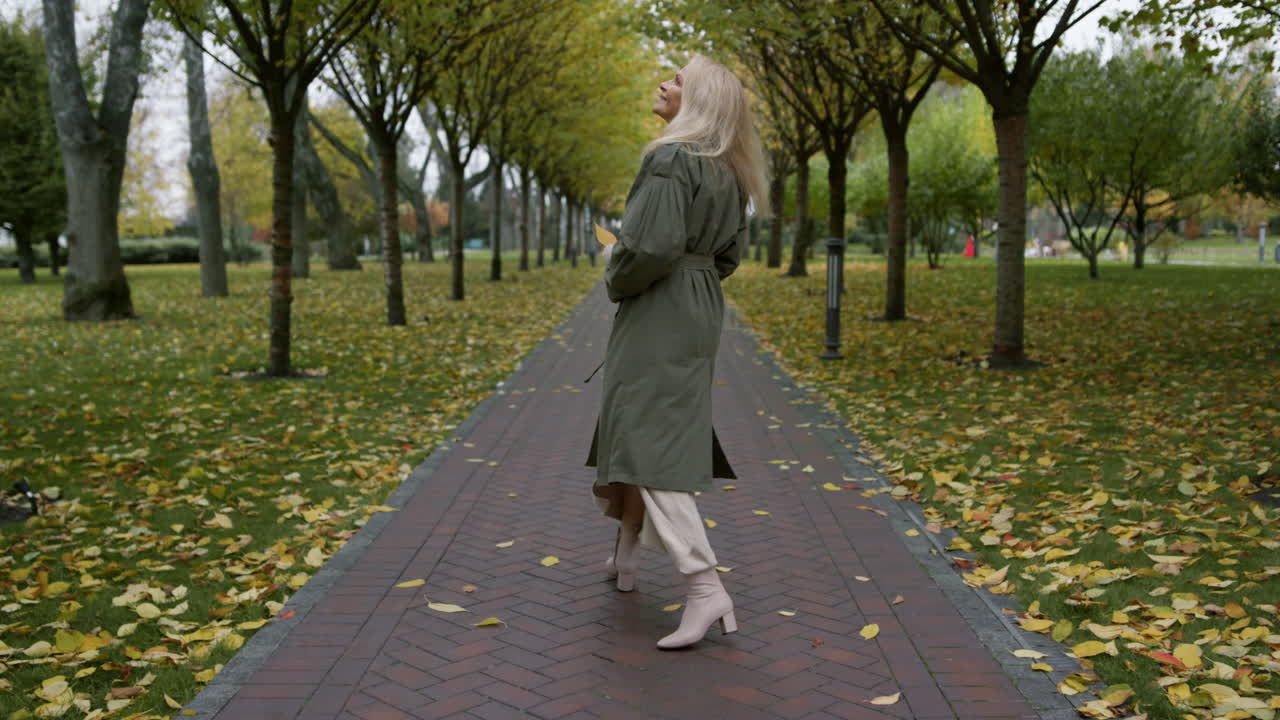 Smiling senior woman having joyful walk in autumn park
