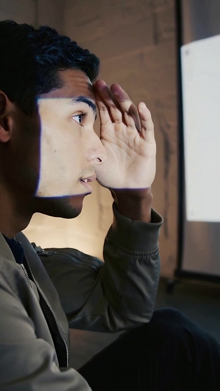 Vertical video: Blocking bright projector light, student in hoodie raising hand at screening room