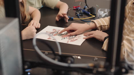 teacher and two teenagers analyzing robot blueprint
