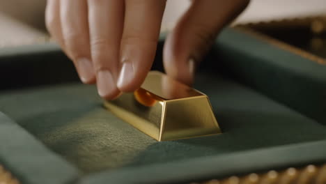 a hand placing a gold bar into a velvet tray