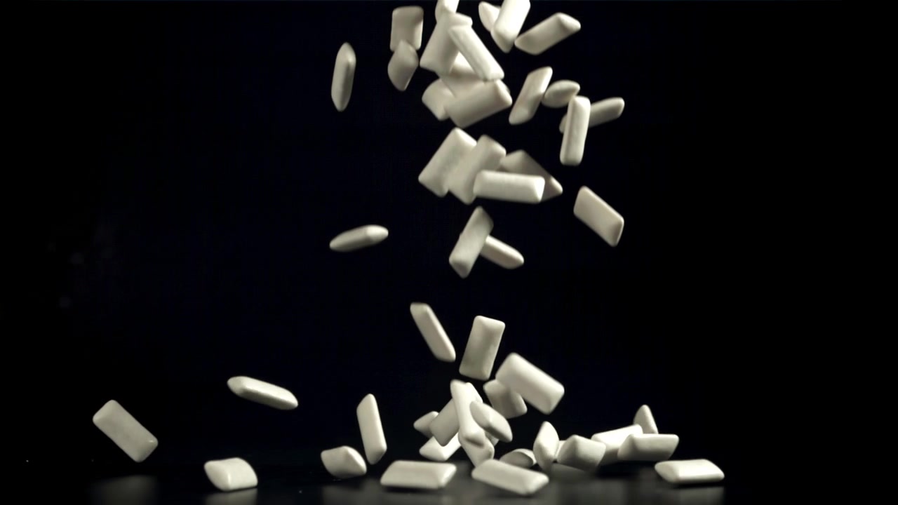 White Chewing Gum Pieces Falling in Slow Motion on Black Background