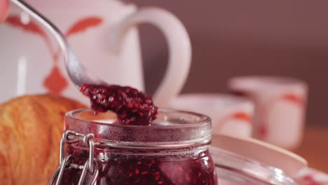 spooning raspberry jam into a jar during breakfast