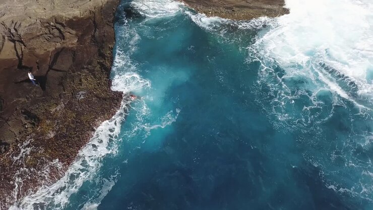 Giovane uomo che nuota verso riva alla Grotta che Sputa a Honolulu, Hawaii - RIPRESA AEREA DALL'ALTO STATICA