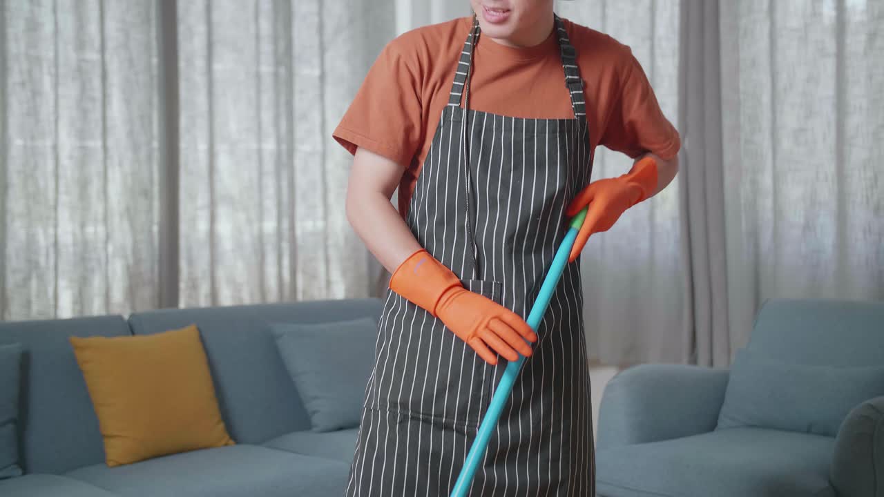 ama de casa asiática con un delantal usando auriculares, escuchando música y bailando mientras limpia el suelo en casa