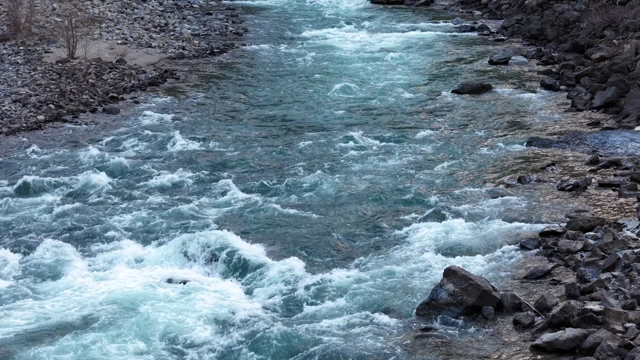 Aerial view of a fast-flowing river with turquoise water and white rapids foaming over rocks in Montana's Rocky Mountains near Glacier National Park