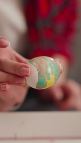 art teacher and little student apply abstract pattern on boiled eggs using ebru technique in studio closeup slow motion. easter holiday ornate preparation