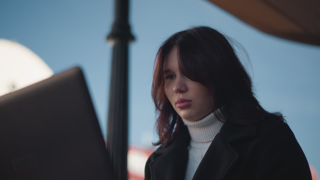 색 타르틀과 검은색 코트를 입고 은 건물과 하늘을 포함한 흐릿한 도시 배경으로 밖에서 앉아있는 여성