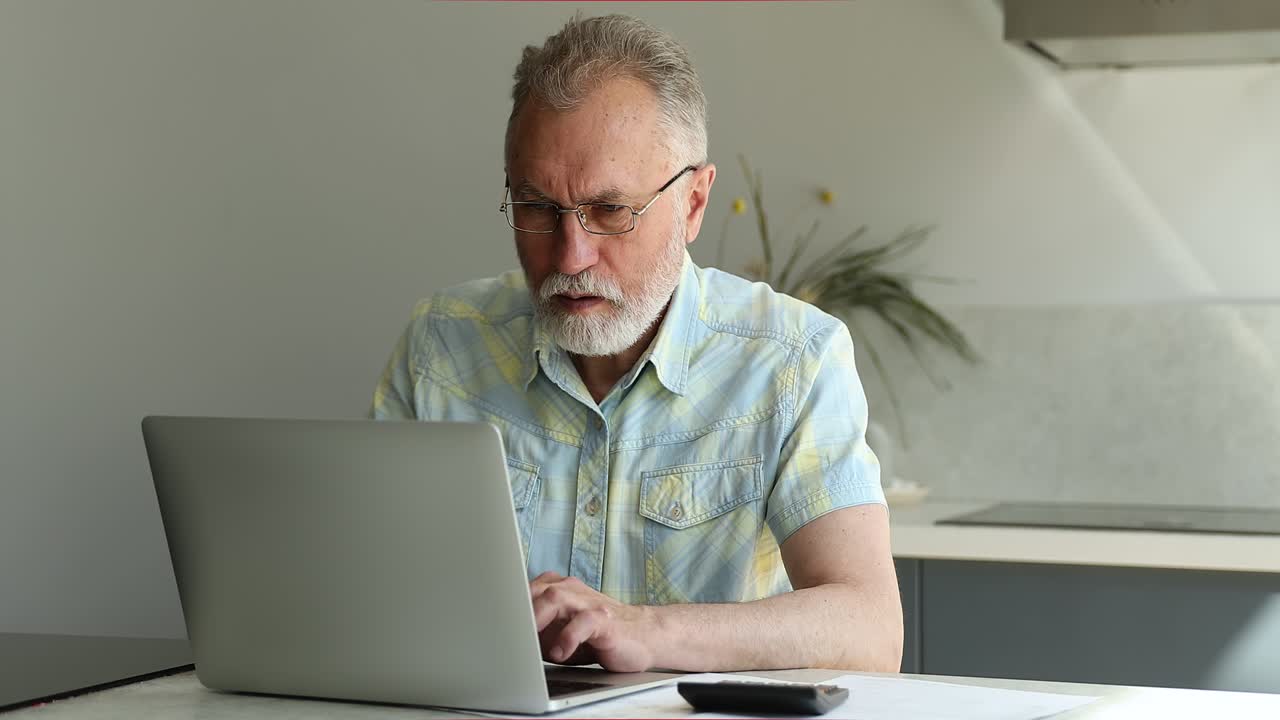 Serious male retiree make home accounting work sitting by laptop