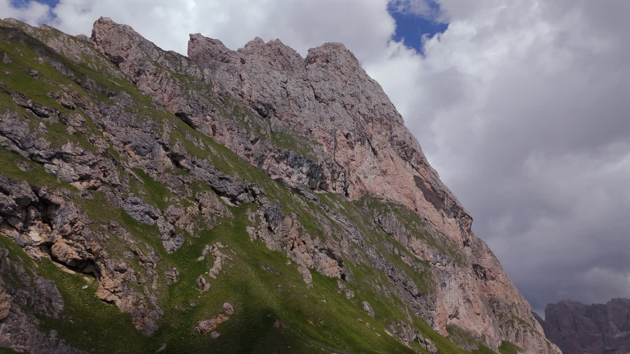 vista aérea detallada de una ladera escarpada y escarpada en las dolomitas, mostrando acantilados rocosos afilados y parches de hierba verde bajo un cielo parcialmente nublado