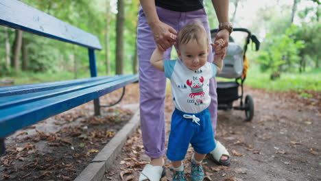 lovely cute caucasian boy walks supported by his mom. little kid stepping with interest and adorable smile. green park backdrop.