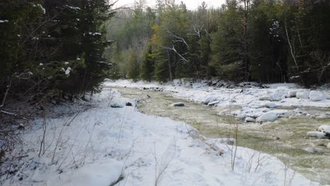 Fließender-Fluss-Mit-Schneebedeckten-Ufern-Und-Dichtem-Immergrünem-Wald-Im-Winter