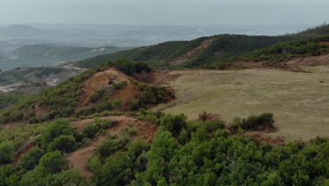 Colorful-hills-with-brown-pastures-and-green-trees-over-city-on-a-foggy-winter-day,-aerial-view