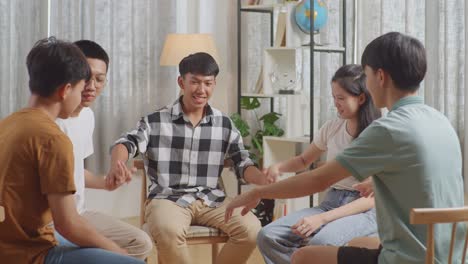 아시안 십대 그룹은 의자에 앉아서 집에서 논의하는 원을 형성합니다. 서로의 손을 잡고, 서로를 지원하고, 손을 들고, 손을 들어 올리는 동기 부여 소리.