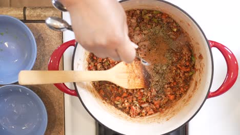 adding red hot cayenne pepper powder to the roux sauce for a spicy gumbo - overhead view slow motion gumbo series