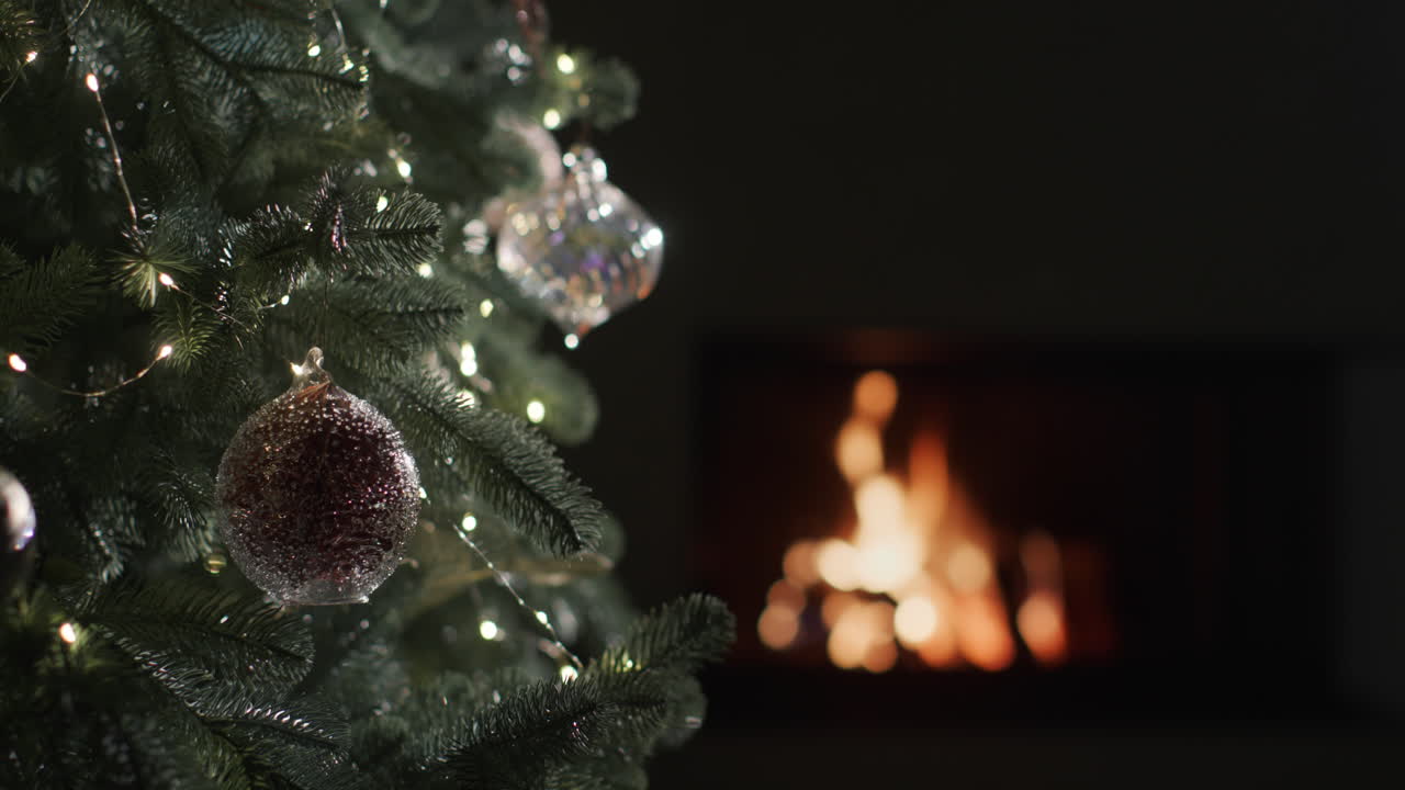 어두운 방의 벽난로에서 불이 난다. 전경의 흐릿한 크리스마스 트리 조명. 4k 슬로우 모션 비디오