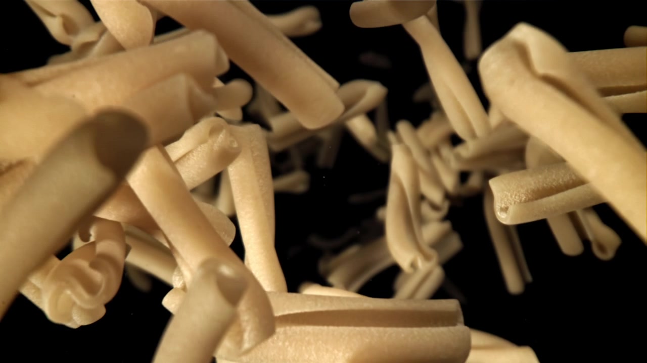 Pasta casarecce cruda che cade al rallentatore su sfondo nero.