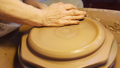 close up of male potter throwing clay for plate onto pottery wheel in ceramics studio