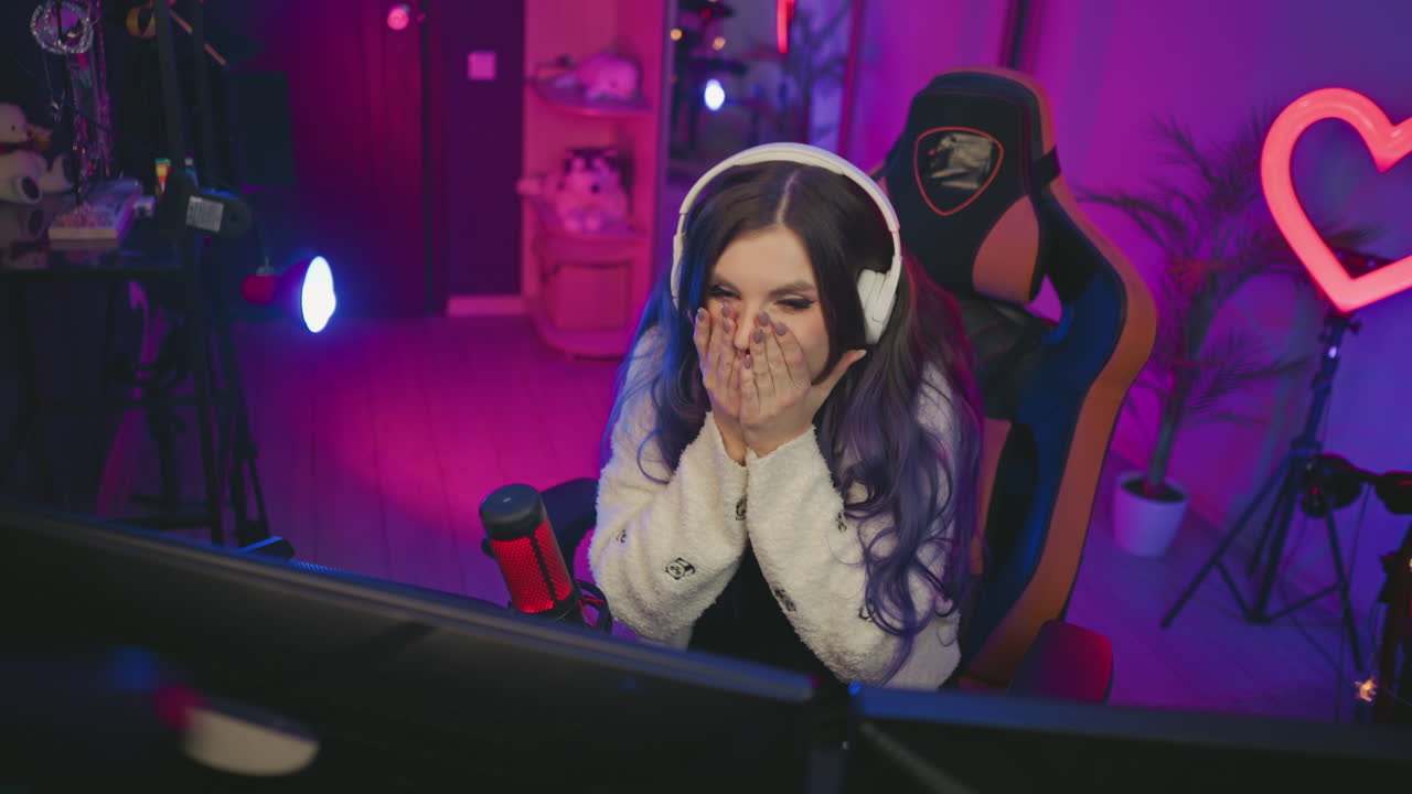 young girl in gaming chair smiling in excitement after winning game, with vibrant purple and pink lights glowing in background and condenser microphone beside dual monitor setup