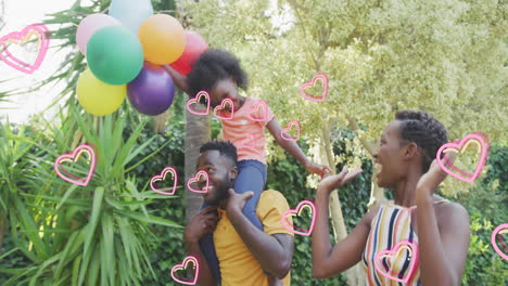 animation of hearts over happy african american family in garden