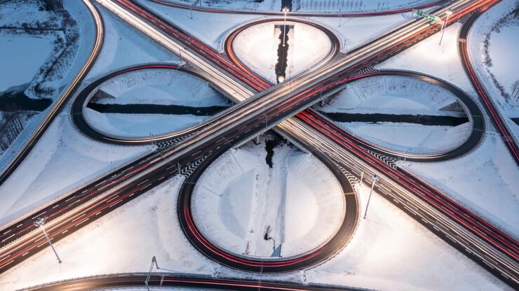 Shifting drone revealing cloverleaf interchange with loop ramps in snow, capturing light trails