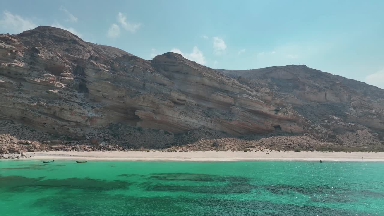 Ripresa aerea in avvicinamento di una scogliera rocciosa e di una montagna lungo la tranquilla costa della spiaggia di Shoab, sull'isola di Socotra nello Yemen