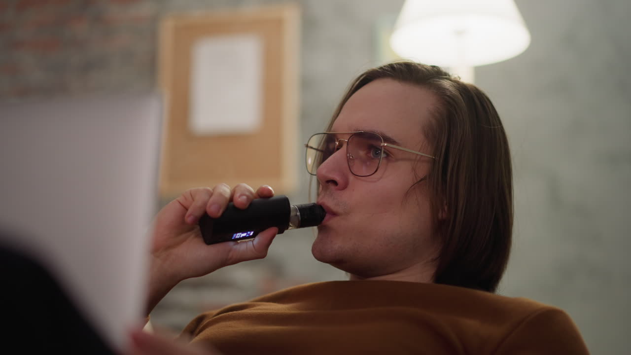 un guapo fanático de los deportes fuma un cigarrillo electrónico viendo baloncesto