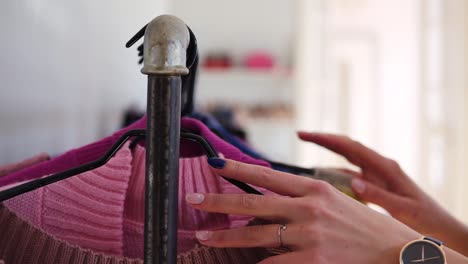 las manos de una mujer joven con manicura de moda corren por un estante de ropa, navegando en una boutique