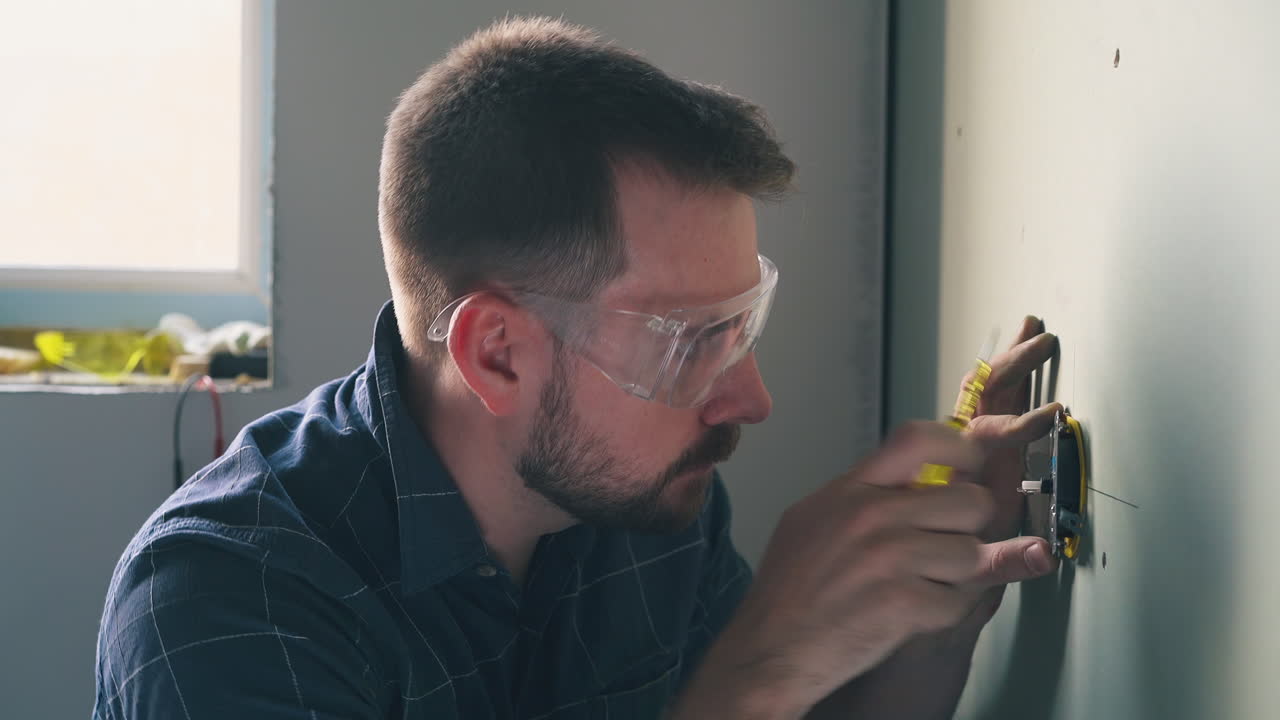 nervous man repairs plug on wall with screwdriver in room