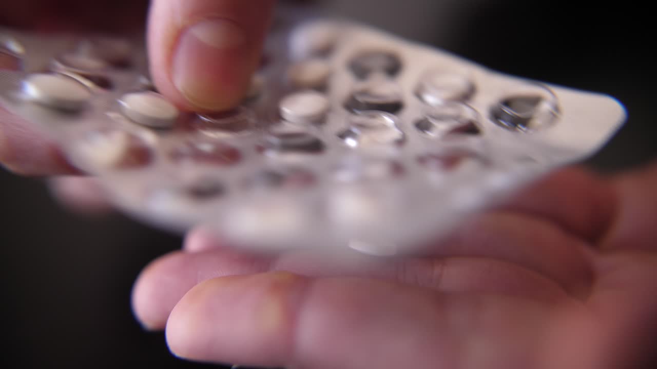 Primer plano de una mano empujando una pastilla blanca de un blíster