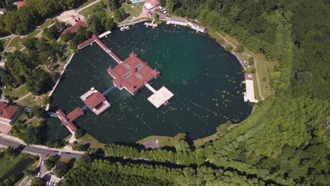 Toma-De-órbita-Aérea-Del-Lago-Héviz-Rodeado-De-Bosque-Verde-En-Hungría