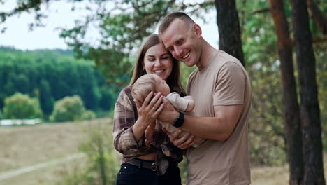 loving couple are focused on their infant they are holding in hands. parents standing in the nature smile to a baby.