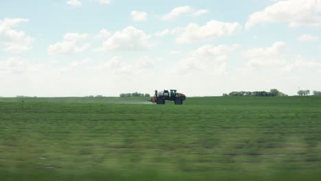 aerial side view, tractor driving fast spraying pesticide on farm crops