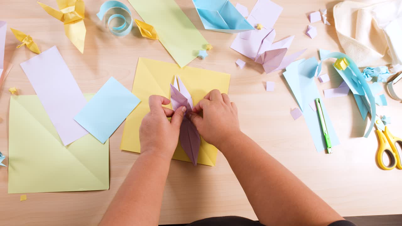 Inquadratura dall'alto di mani che piegano con cura un foglio di carta viola per creare un uccello origami su una scrivania