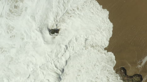 toma aérea descendente en cámara lenta del océano chocando contra una roca en una playa