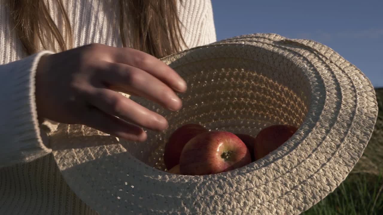 mujer mostrando manzanas rojas en un sombrero de paja plano medio