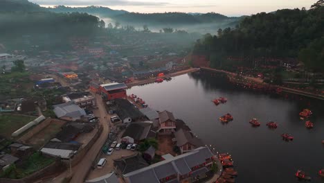 seguimiento aéreo de drones a la izquierda de la aldea de ban rak thai, tailandia, ubicada entre un tranquilo lago y montañas cubiertas de niebla alrededor de las casas