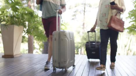 diverse senior couple walking with luggage to a house in sunny outdoors