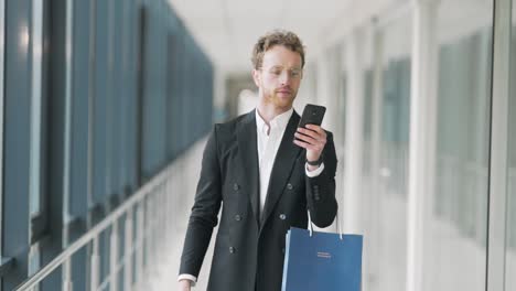 hombre adulto guapo caminando por el pasillo con bolsas de compras y un teléfono inteligente