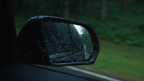 close up of a side view mirror of a black car on a rainy day