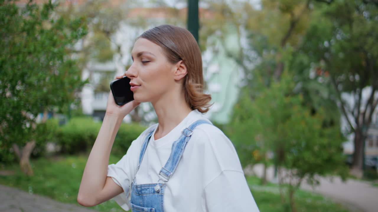 Young woman talking mobile phone walking urban park closeup. Carefree girl