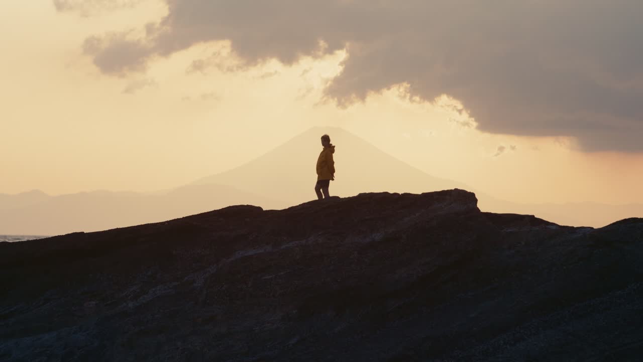 Golden Hour Reflections by the Sea in Japan
The wind moves gently as a woman faces crashing waves on a rugged coast, bathed in epic sunset light.