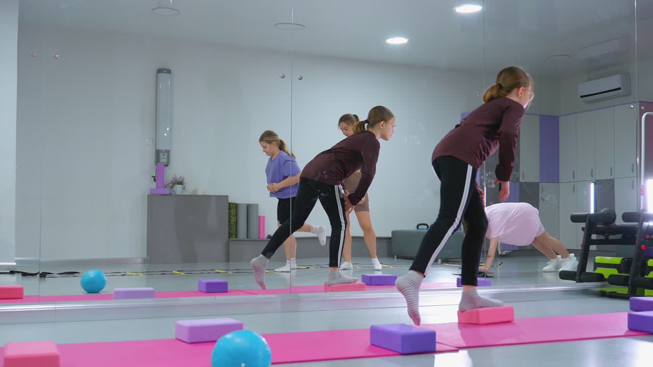 niños involucrados en una sesión de entrenamiento realizando ejercicios de equilibrio y coordinación mientras el supervisor observa, el entorno del gimnasio incluye esteras de ejercicio, bloques de estabilidad y varios equipos de fitness