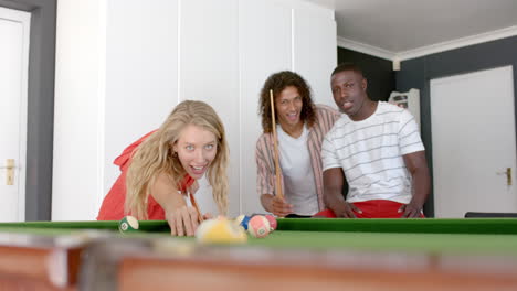 young caucasian woman plays pool at home, flanked by friends