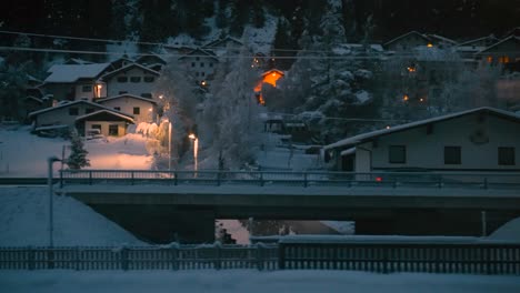 Casas-De-Pueblo-Cubiertas-De-Nieve-Por-La-Noche-Durante-El-Invierno-Vistas-A-Través-De-Un-Vehículo-De-Viaje