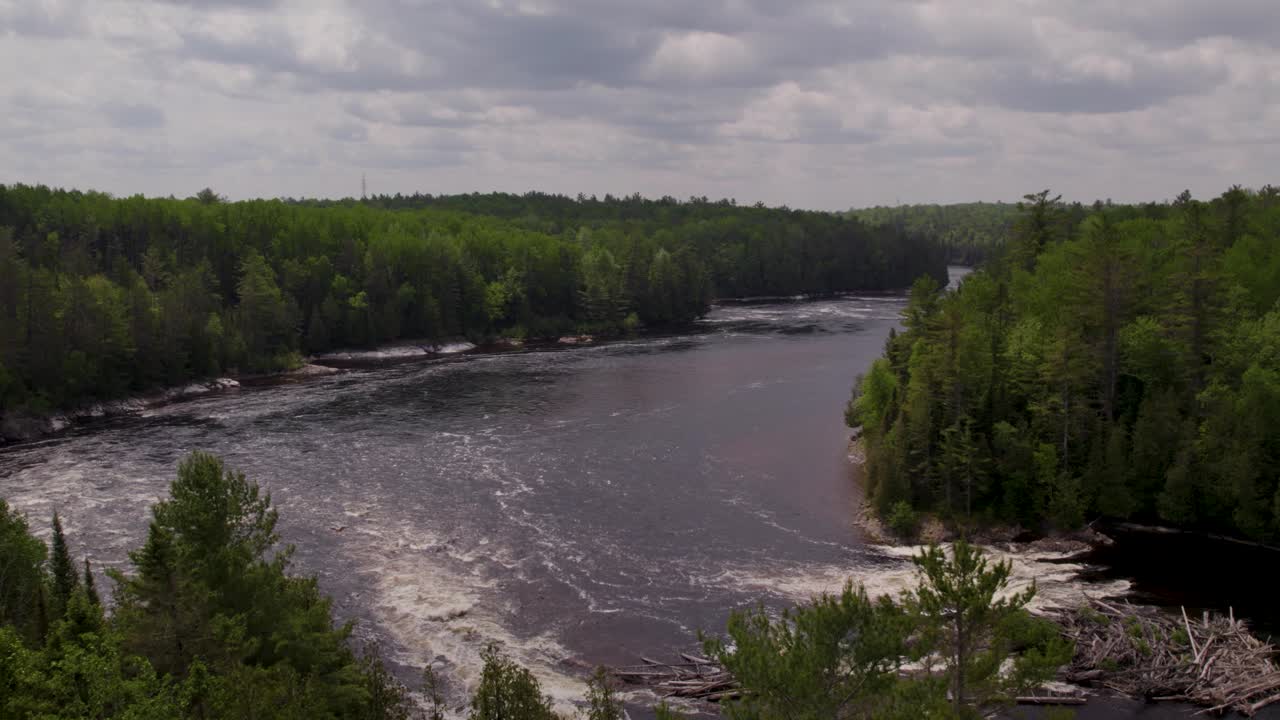 Luftfoto af en hurtigtstrømmende flod med drivtømmer på Gatineau-floden midt i fyrreskove