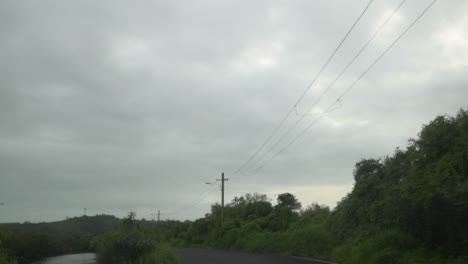 Toma-Pov-De-Un-Vehículo-Que-Viaja-A-Lo-Largo-De-Una-Carretera-Asfaltada-Con-Una-Línea-Eléctrica-Aérea-Que-Corre-A-Lo-Largo-De-La-Carretera-En-Un-Día-Nublado-Gris-Y-Sombrío,-Panjim,-India