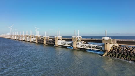 toma aérea en cámara lenta de la barrera contra la marejada ciclónica del este de scheldt y turbinas eólicas en zelanda, los países bajos en un hermoso día soleado con un cielo azul